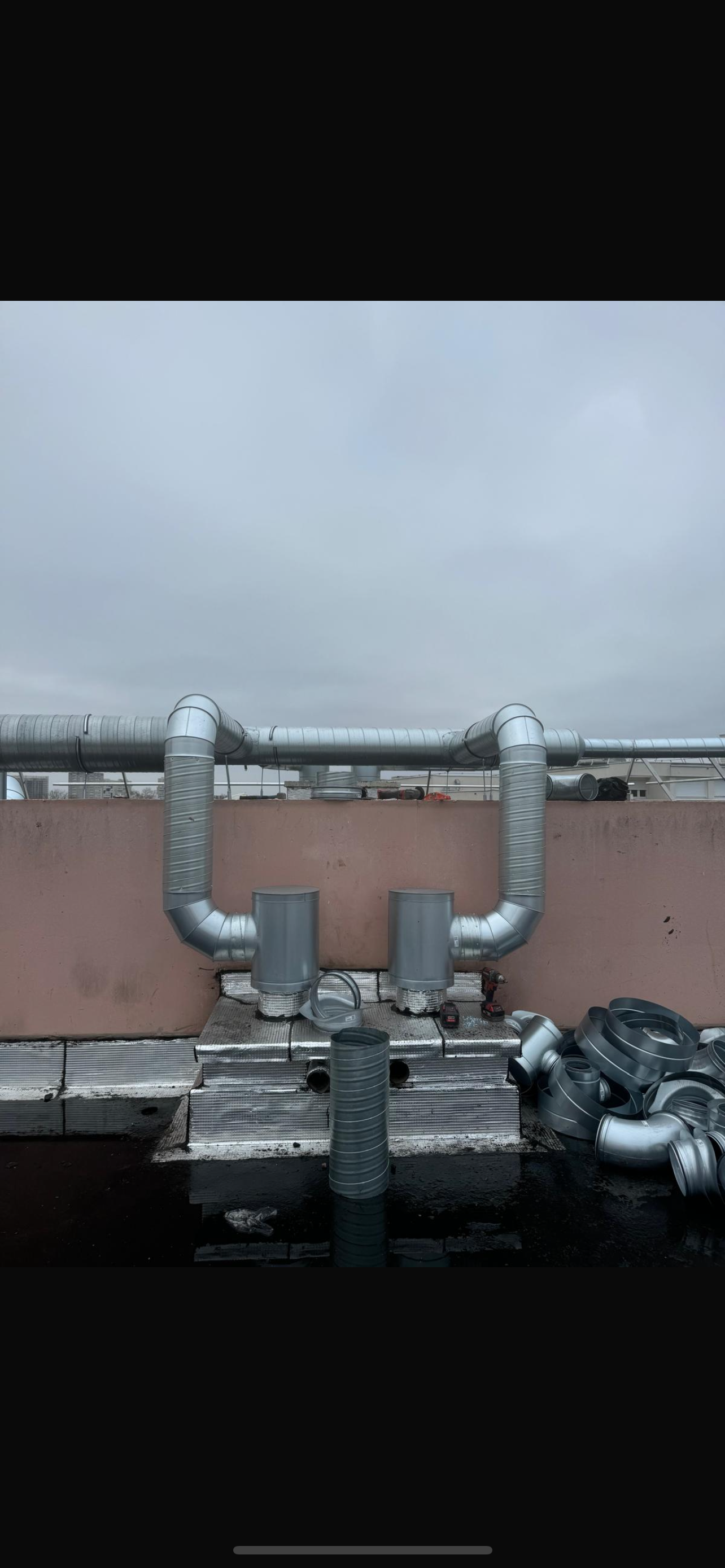 Tuyaux et vannes industriels sur un toit sous un ciel gris nuageux, avec vue lointaine sur le front de mer.