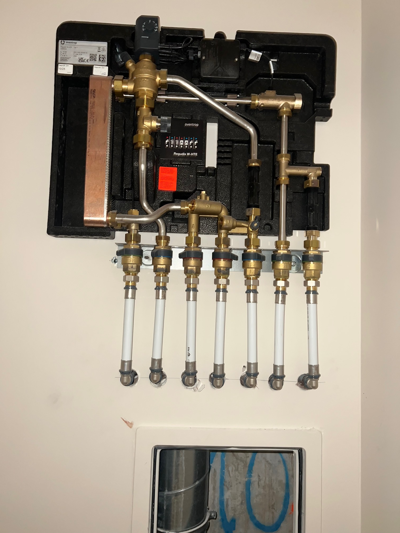 Collecteur de plomberie mural avec vannes en laiton et six raccords de tuyau au-dessus d'un petit panneau utilitaire