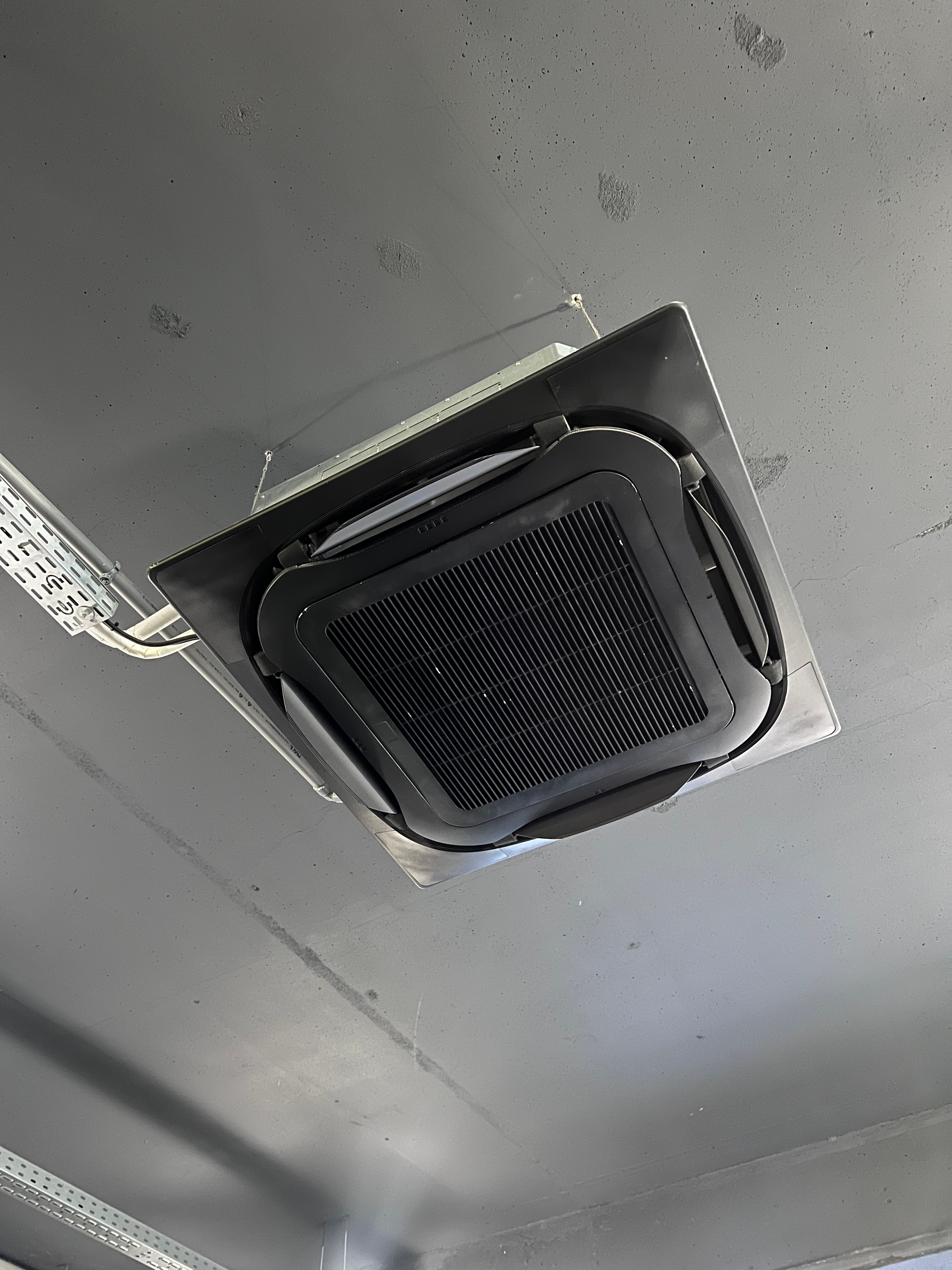 Grille d'aération ou haut-parleur noir fixé au plafond, intégré à une surface métallique grise.