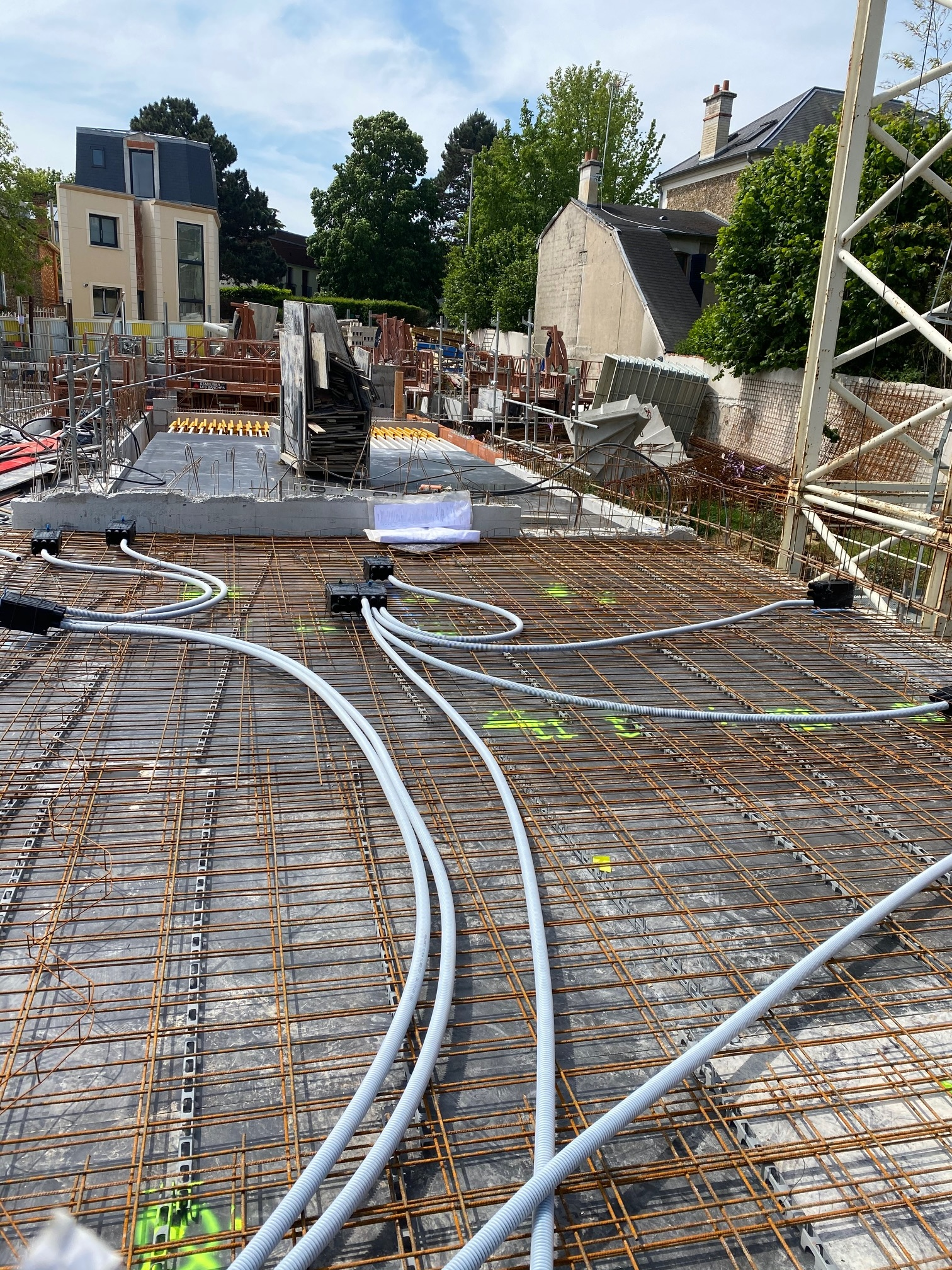Chantier de construction avec treillis d'armature, tuyaux blancs enroulés et échafaudages dans une cour