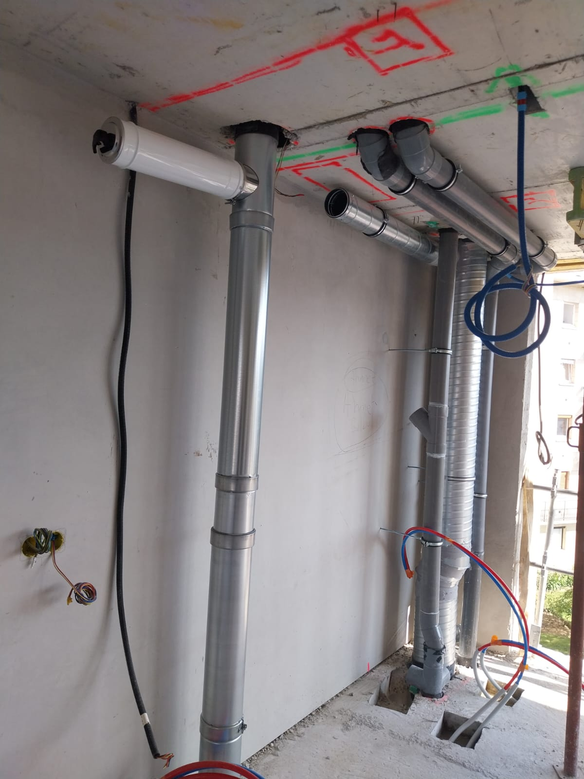 Mur intérieur en construction avec tuyaux en PVC gris apparents, câbles et marquages ​​au plafond dans une pièce inachevée