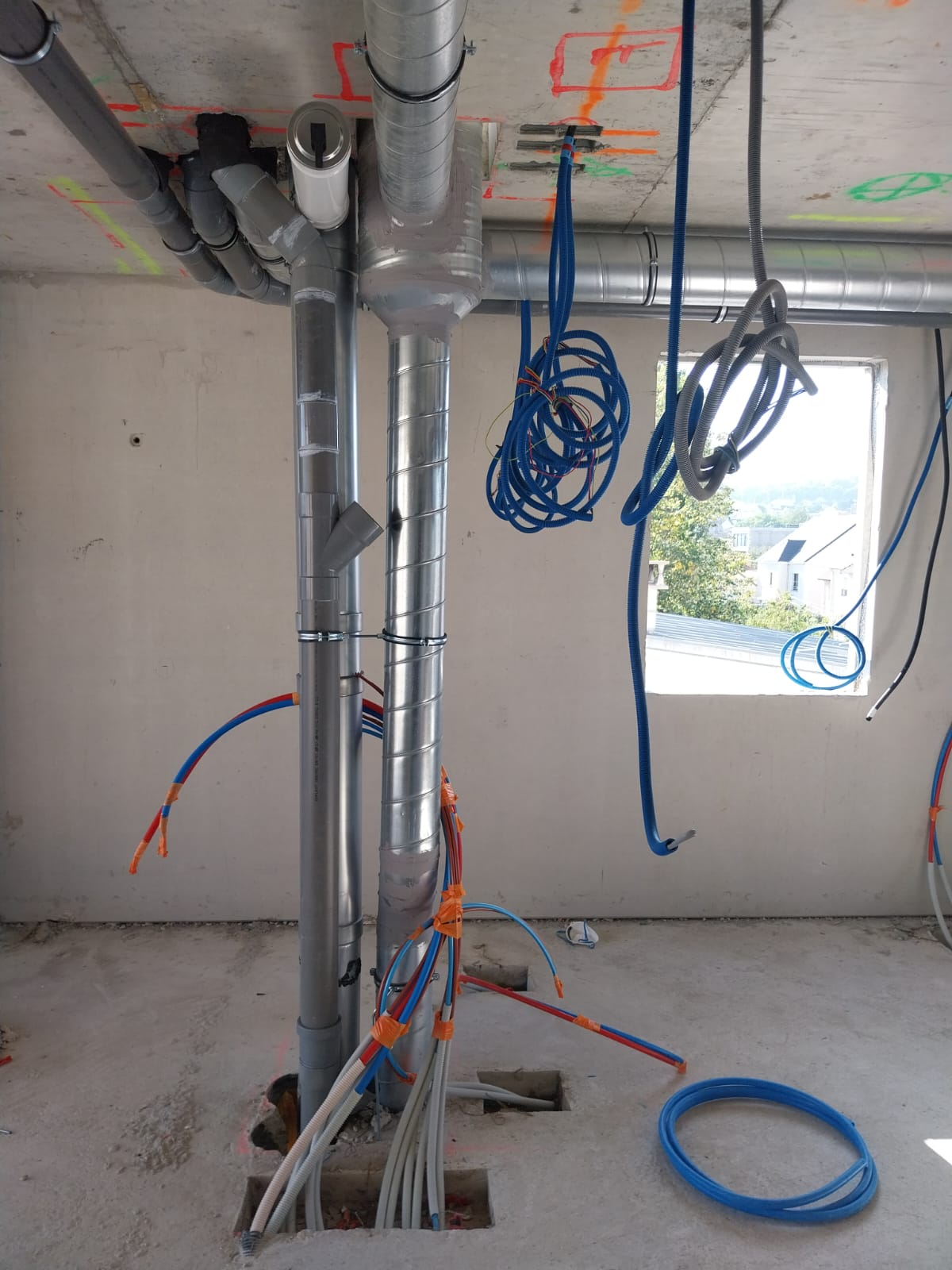 Intérieur inachevé avec tuyaux apparents et câbles électriques pendant du plafond près d'une ouverture de fenêtre