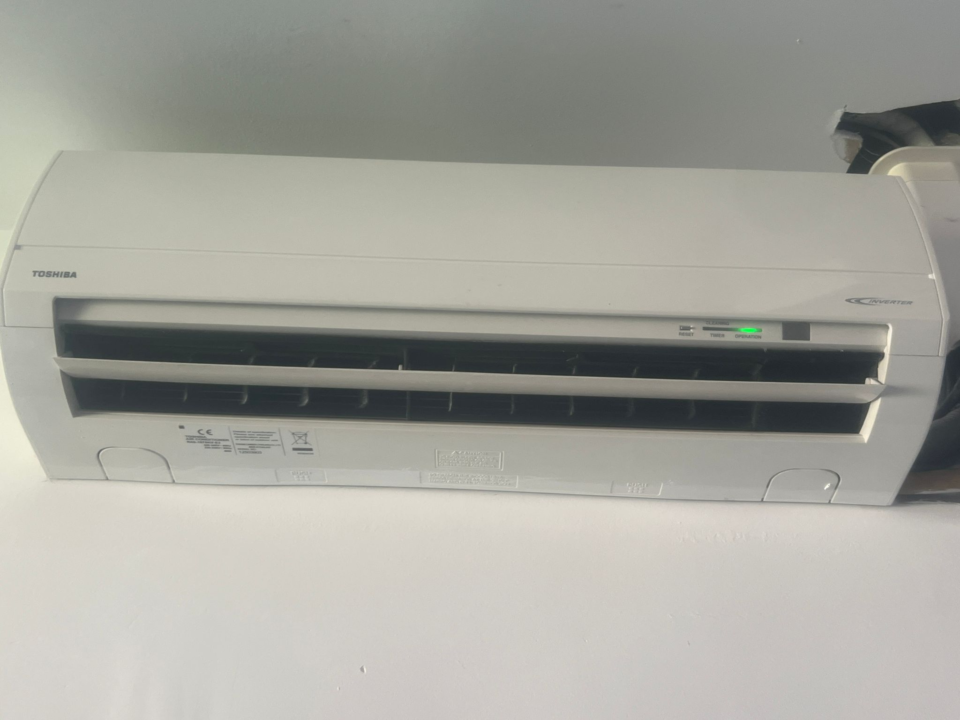Climatiseur mural blanc avec grilles d'aération et voyant vert