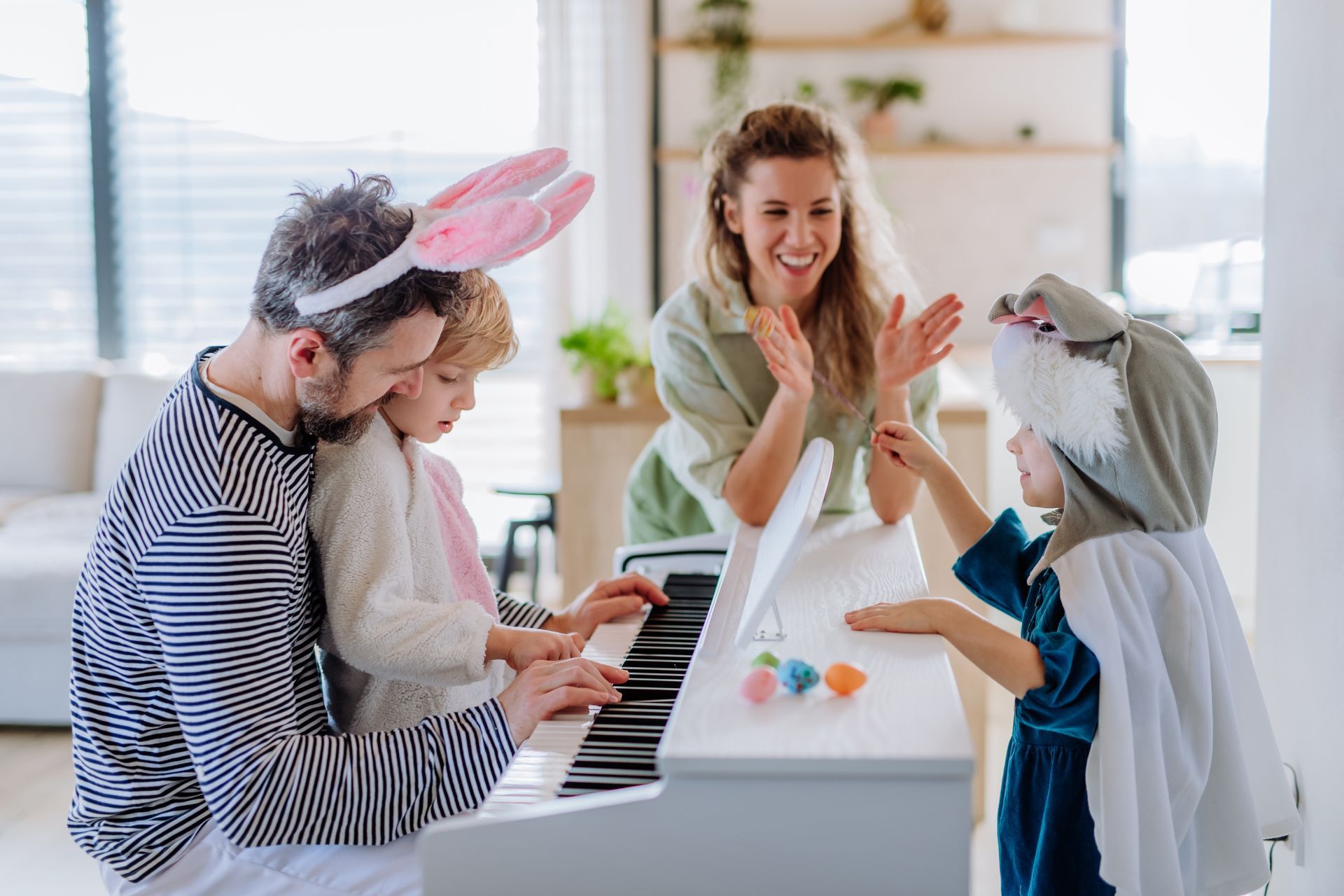 Family in Easter costumes plays piano. The woman claps. A child wears a bunny costume.