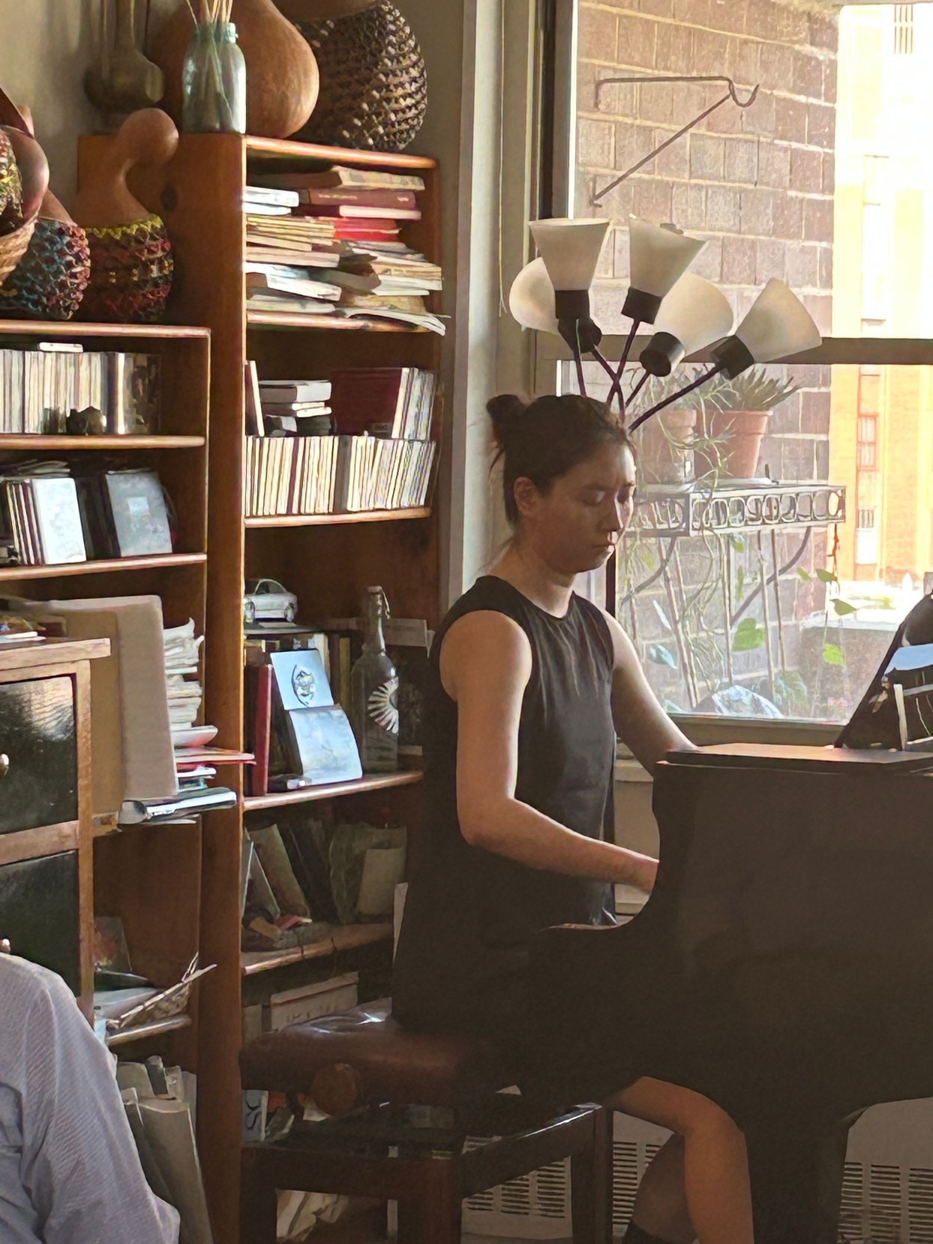 Person playing piano in a cozy room with shelves and a large window.