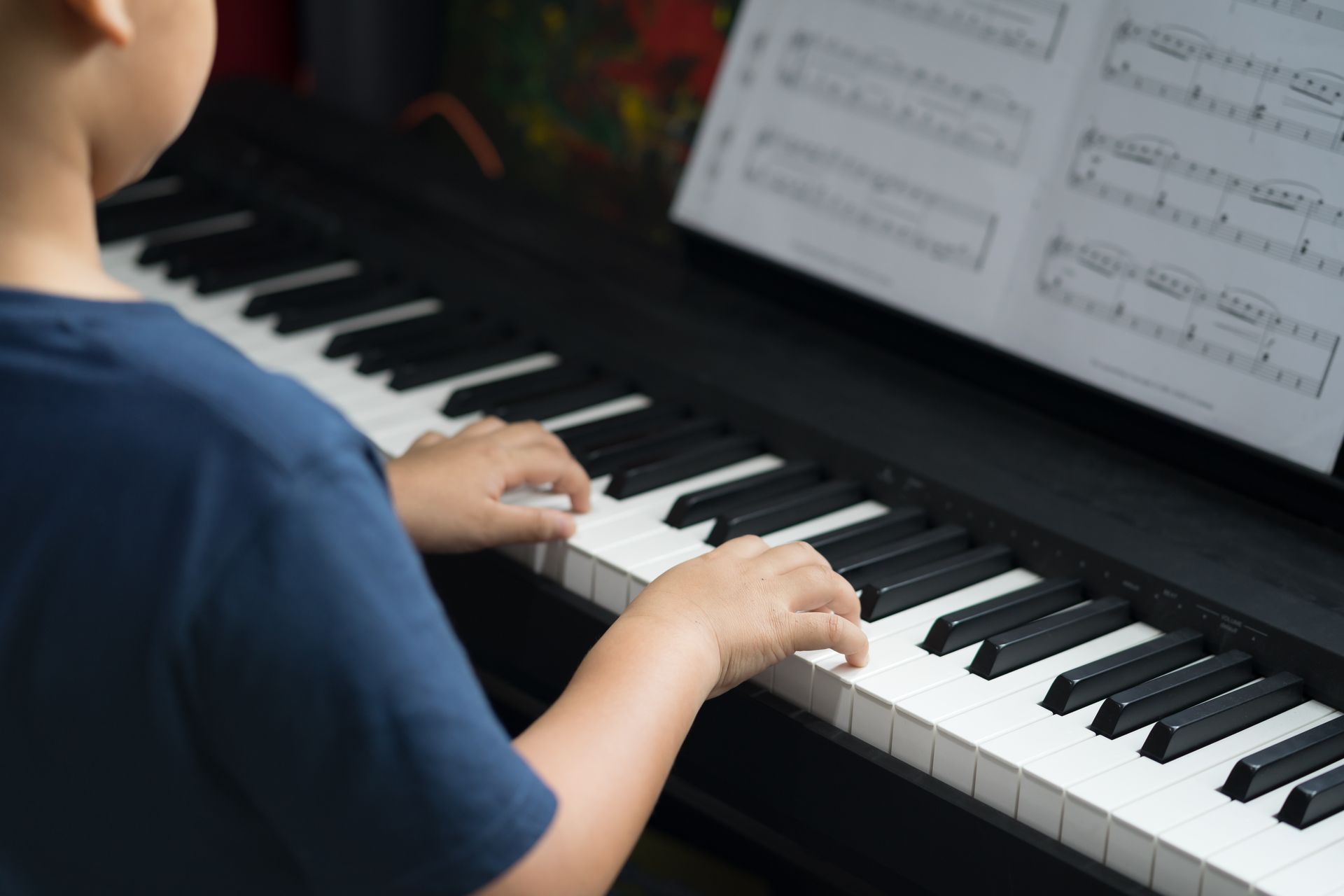 Child playing a black piano, hands on the keys with sheet music on the stand