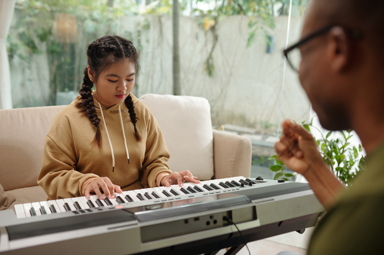 Person playing a keyboard while another listens nearby in a bright living room