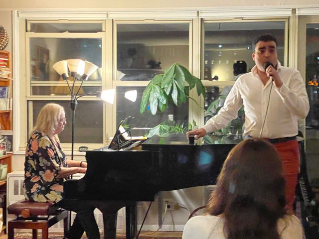Singer and pianist performing in a cozy indoor venue, with audience visible in foreground.