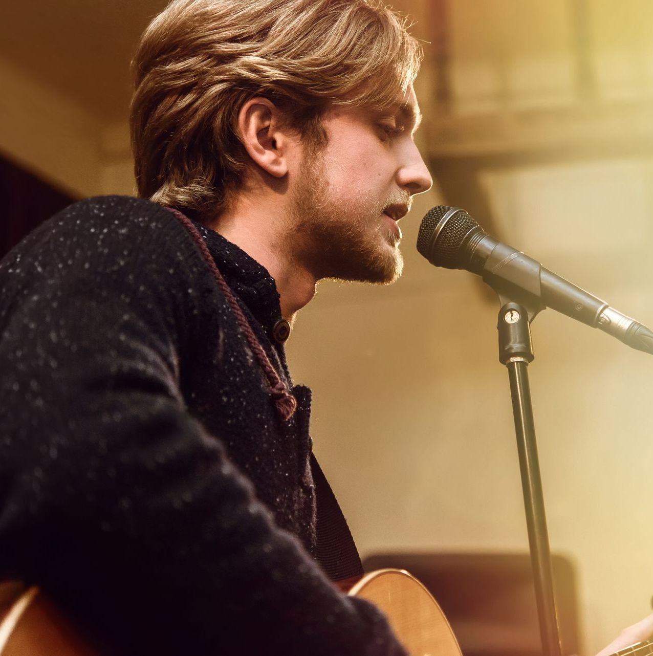 A man singing into a microphone while playing a guitar
