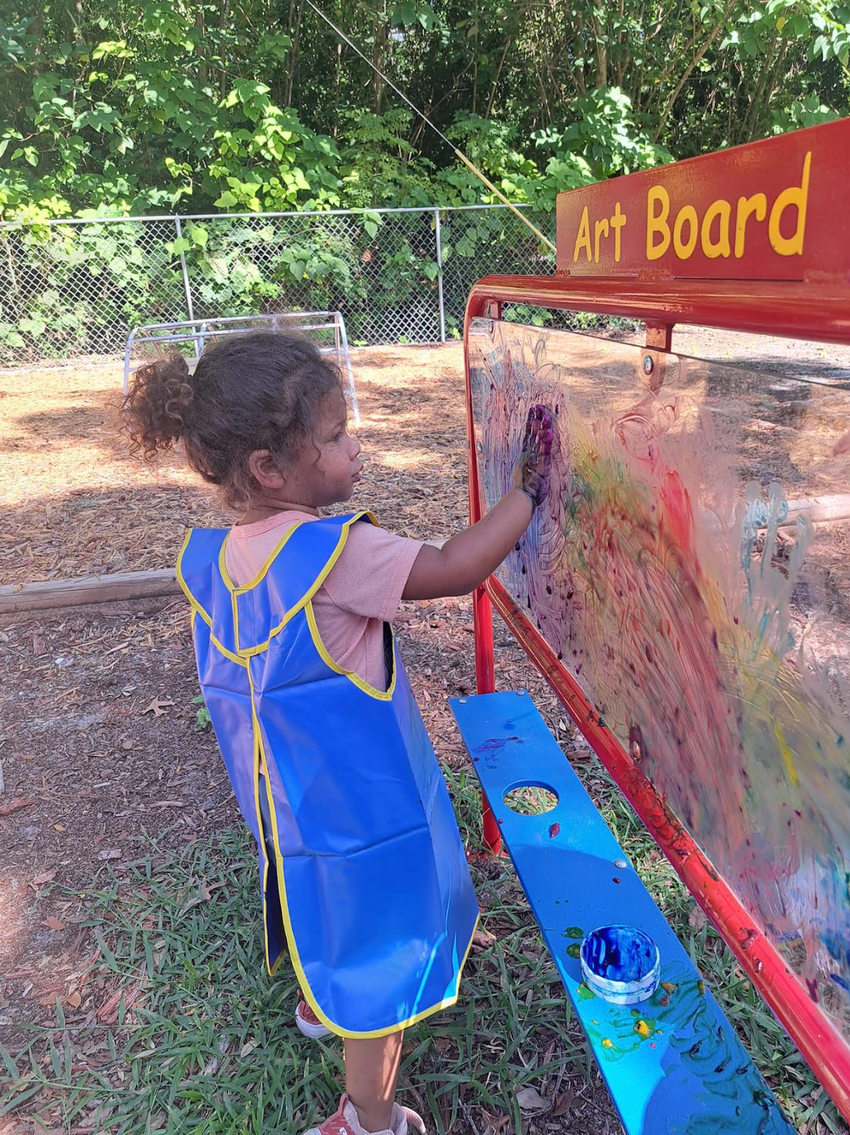 A little girl is painting on an art board outside.