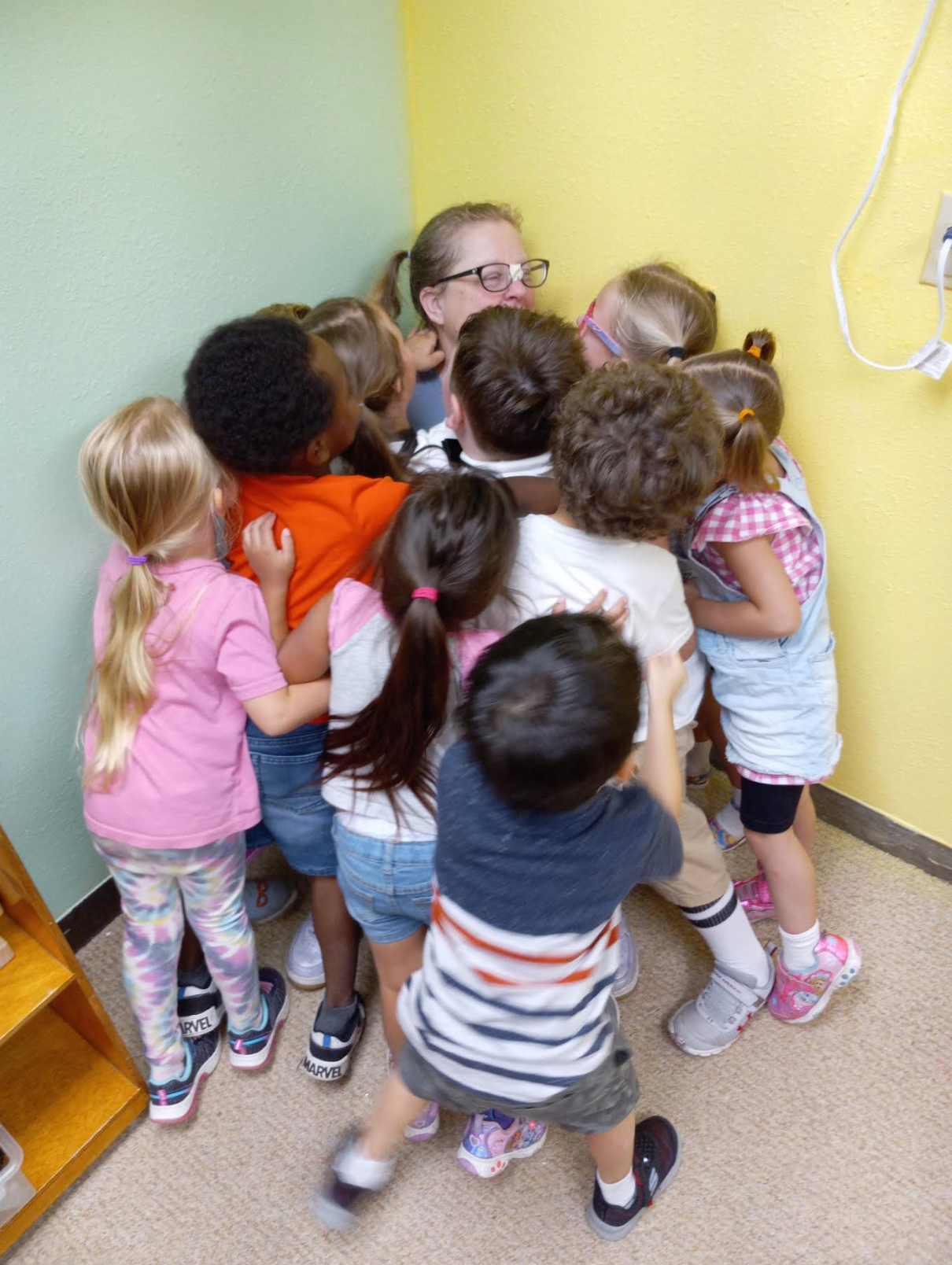 A group of children are hugging a woman in a room.