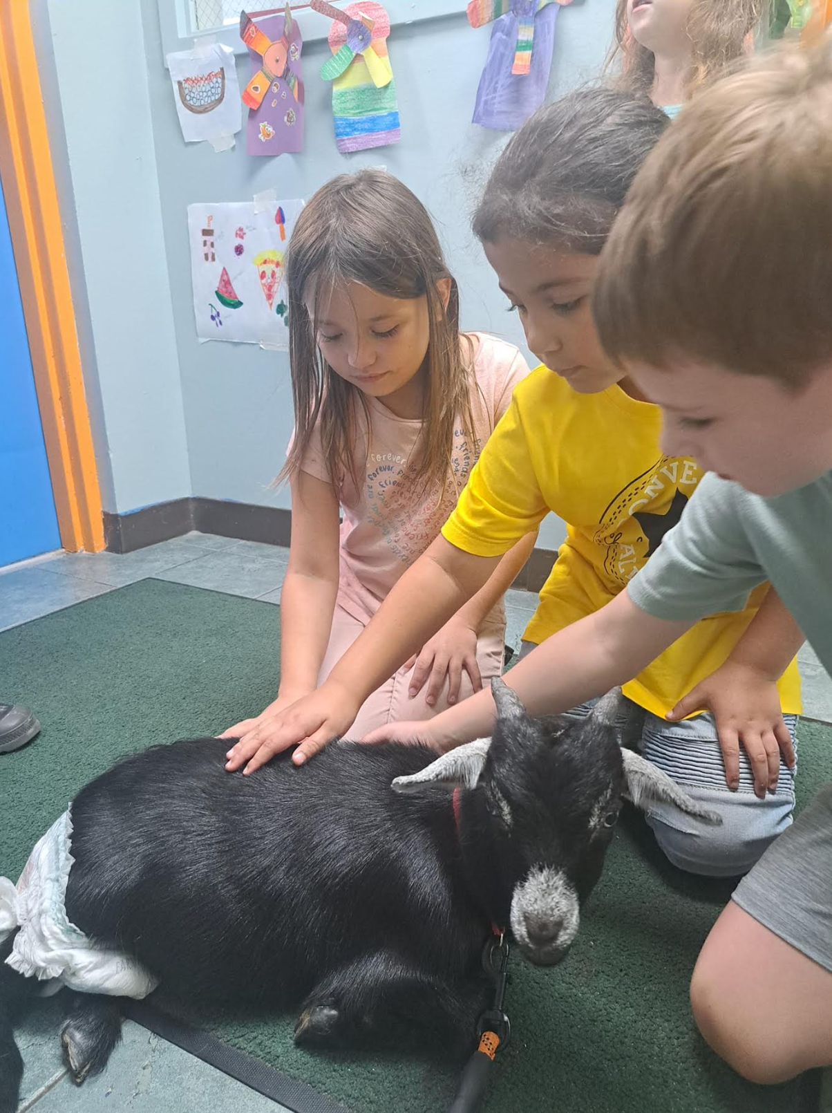 A group of children are petting a goat on the floor.