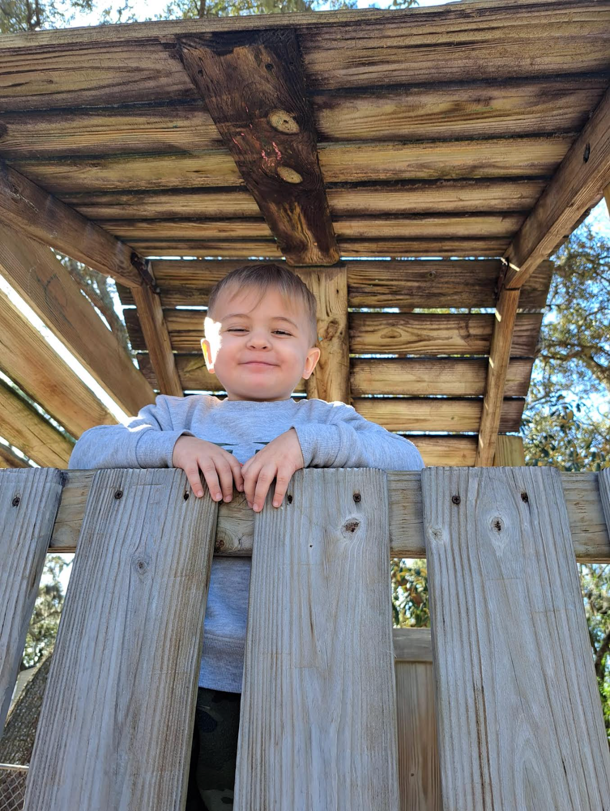 A young boy is leaning over a wooden fence.