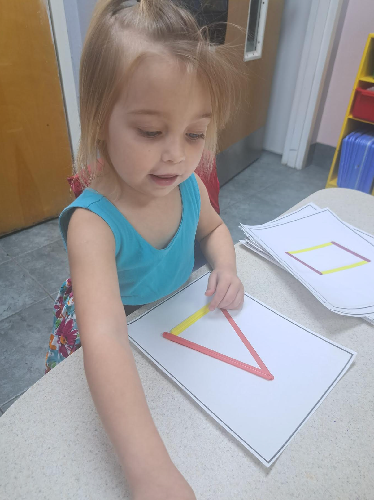A little girl is drawing a triangle on a piece of paper