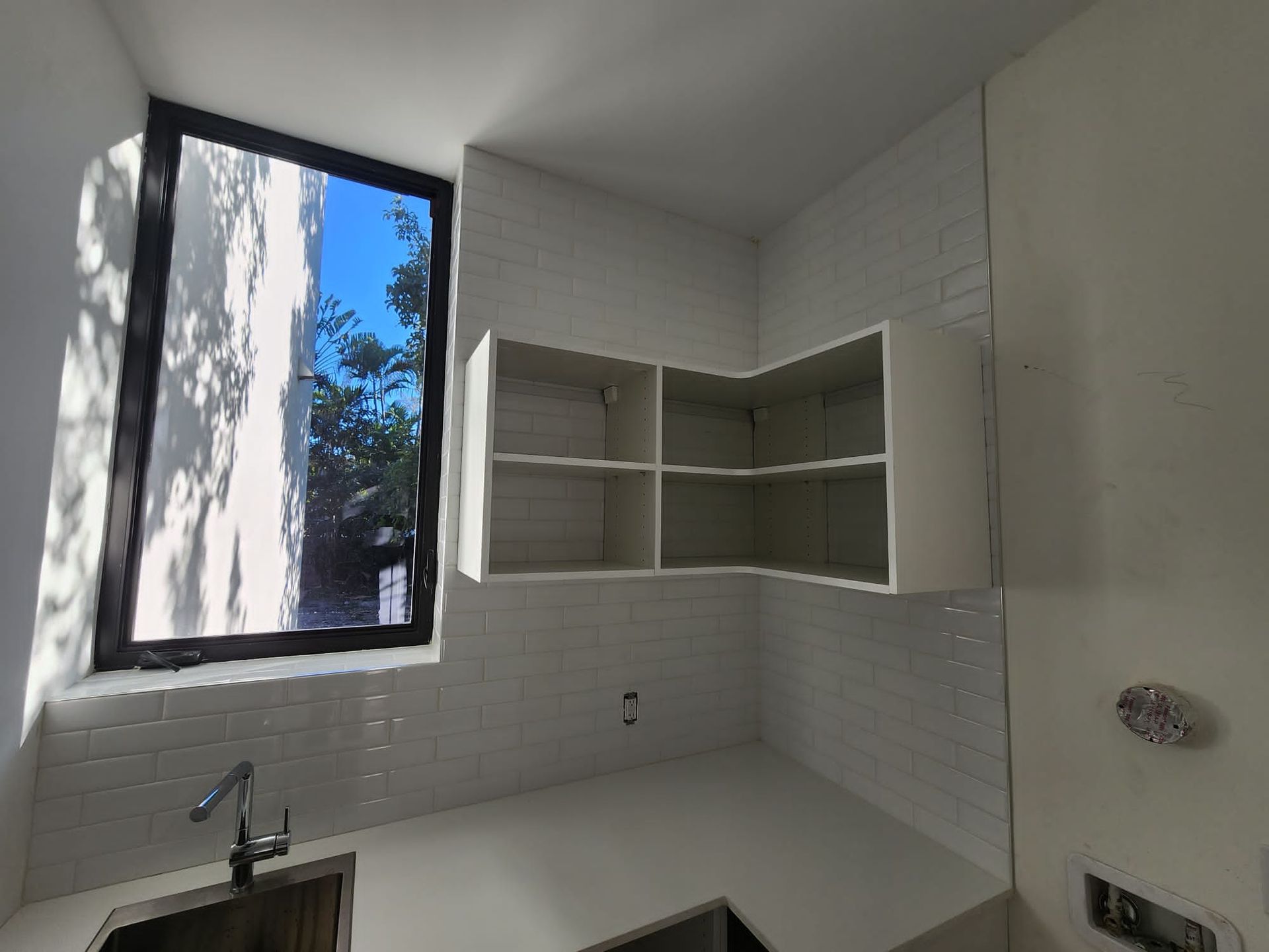 A kitchen with a sink , shelves and a window.