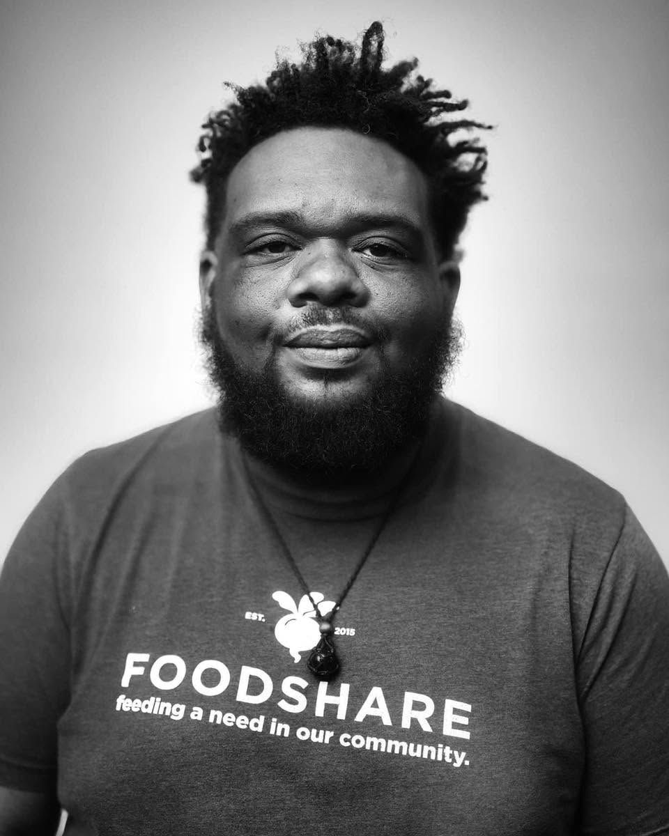 Man in dark T-shirt with “FOODSHARE” logo, facing camera against a plain light background