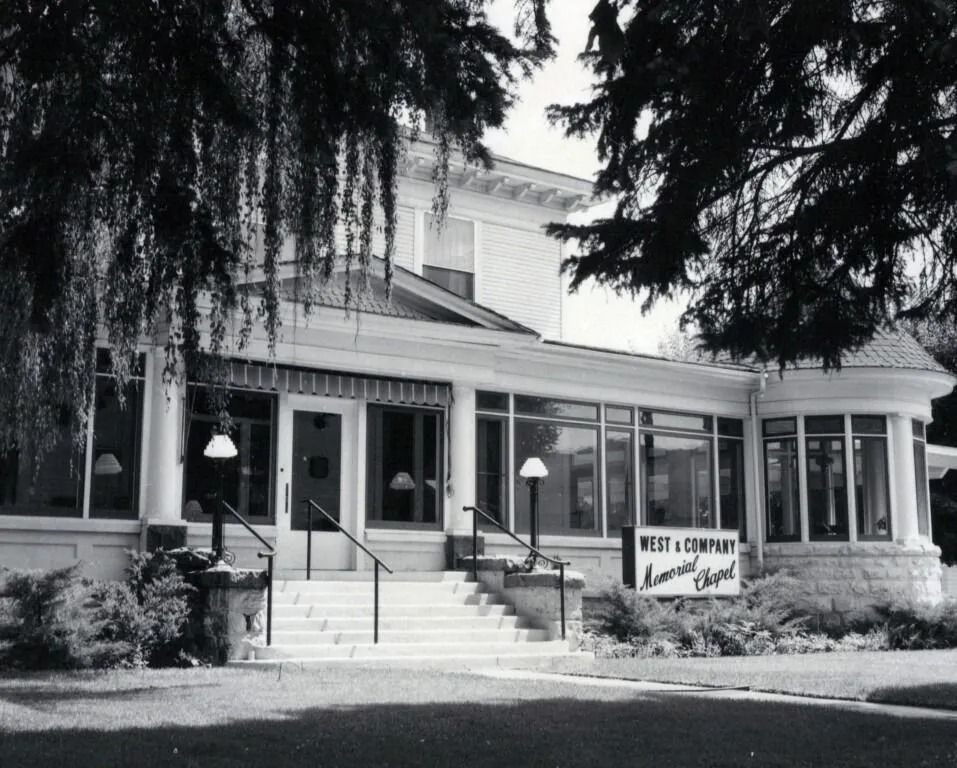 A historic building with columns, steps, and a covered porch, surrounded by trees.