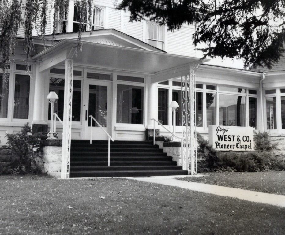 Black-and-white view of West & Co printer shop with a front porch, stairs, and sign by the entrance