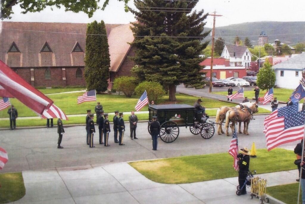 Horse-drawn hearse procession with U.S. flags outside a church on a cloudy day