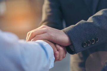 Two people shaking hands, one in a dark suit and one in a light shirt.