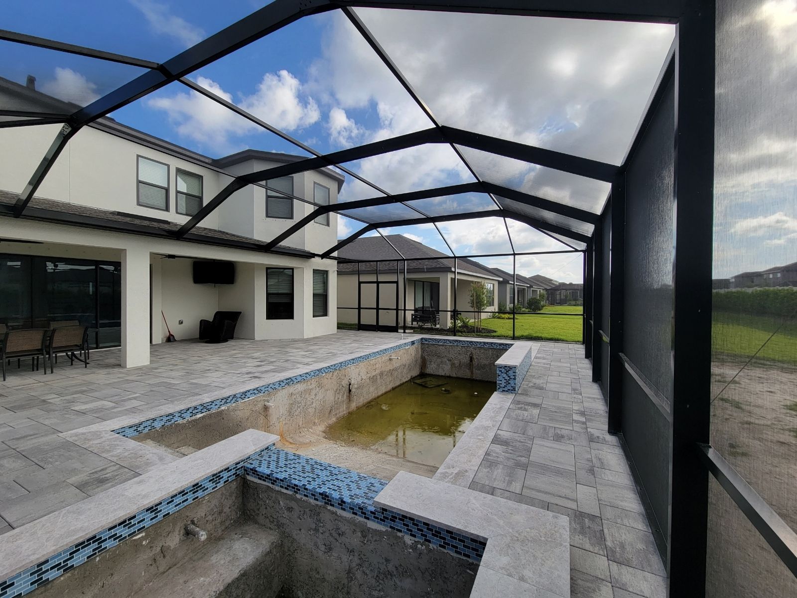 Screened patio with a rectangular pool and stone deck beside a modern house under a partly cloudy sky