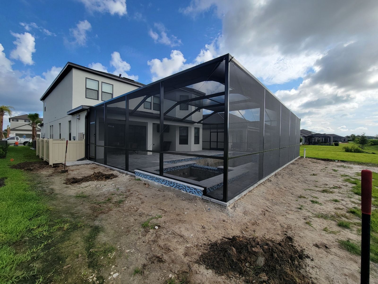 Modern house with a large screened enclosure over a patio, seen from a sandy yard under a cloudy sky.