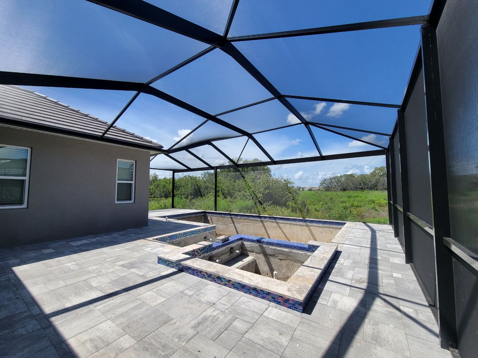 Screened patio with blue net roof and a rectangular in-ground fire pit beside a house.
