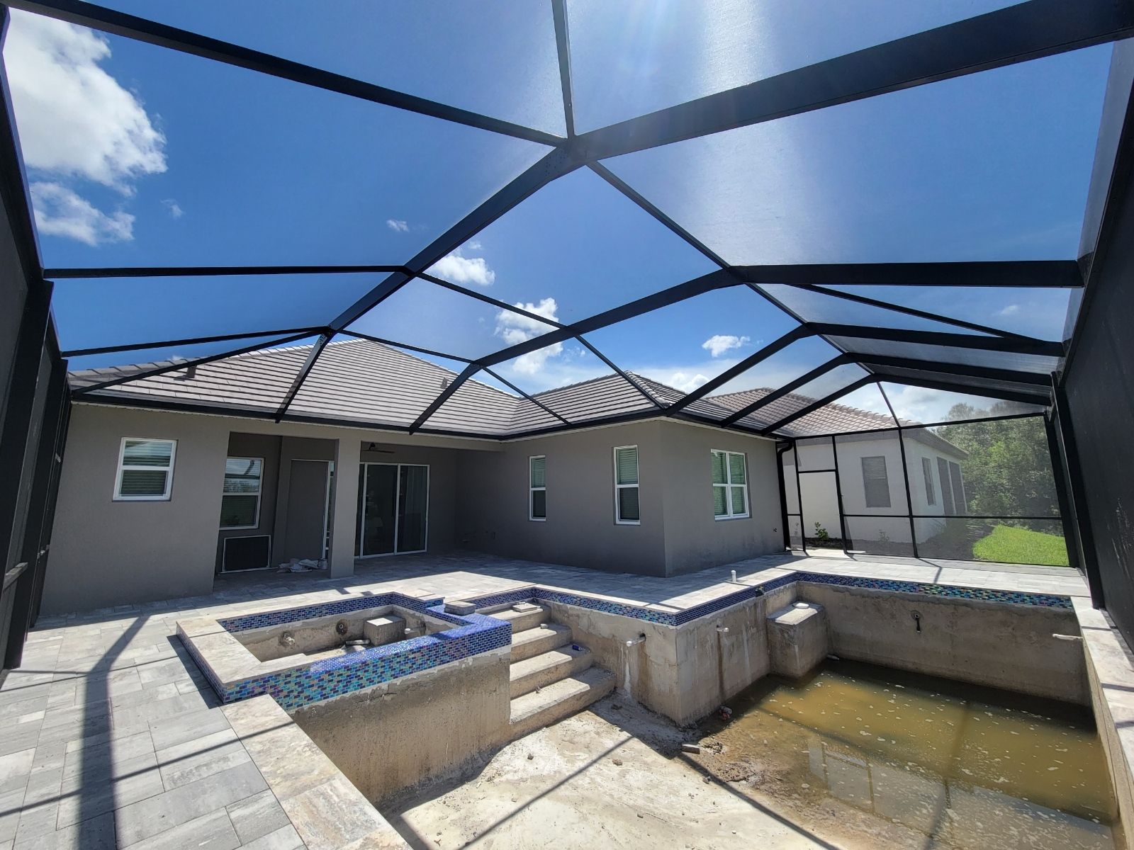 Backyard patio with screened enclosure, empty pool, and beige house under a blue sky