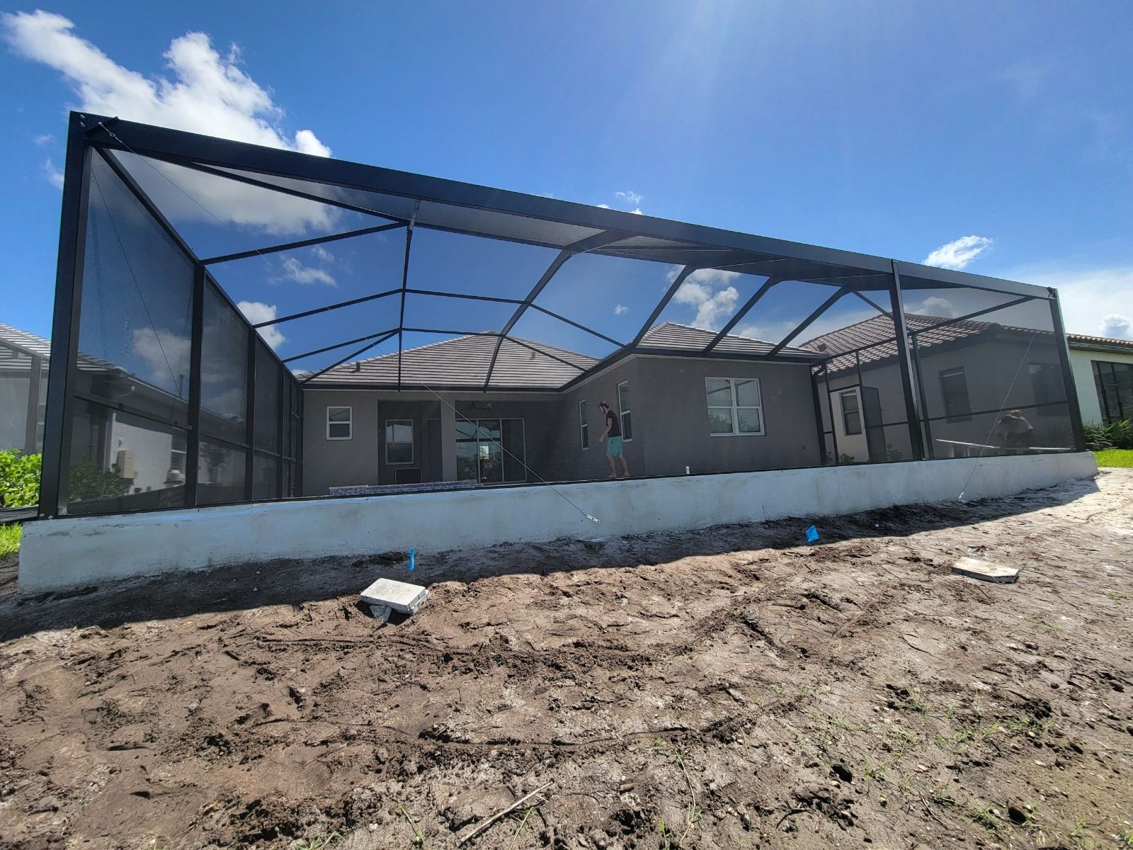 Partially built screened patio with gray walls, black frame, and dirt foreground under a blue sky