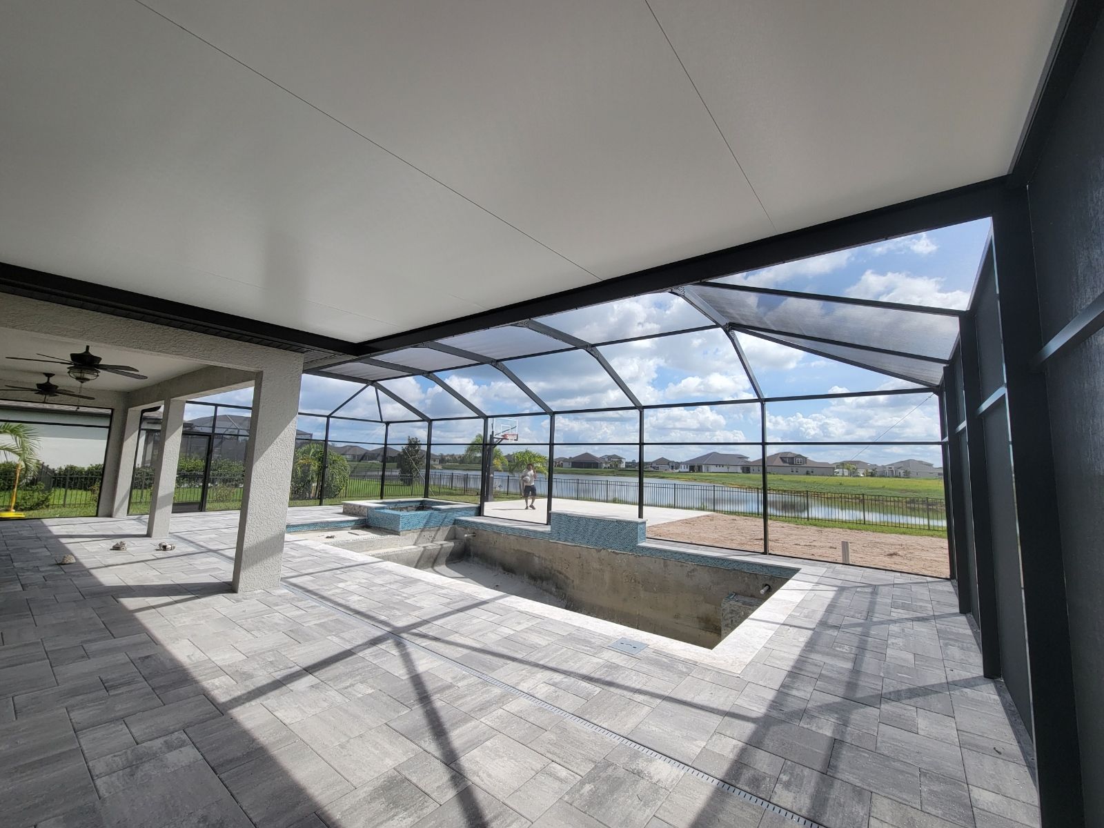 Covered patio with a screened-in pool enclosure, tiled floor, and open view of fields beyond.