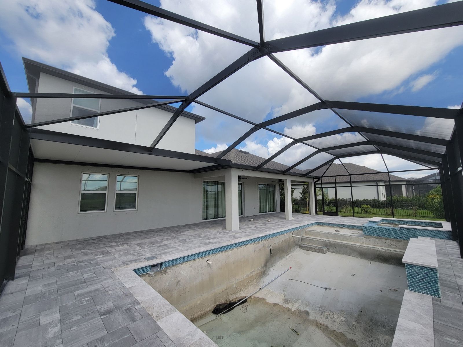 Outdoor patio with a screened enclosure around a partially empty swimming pool and gray stone deck