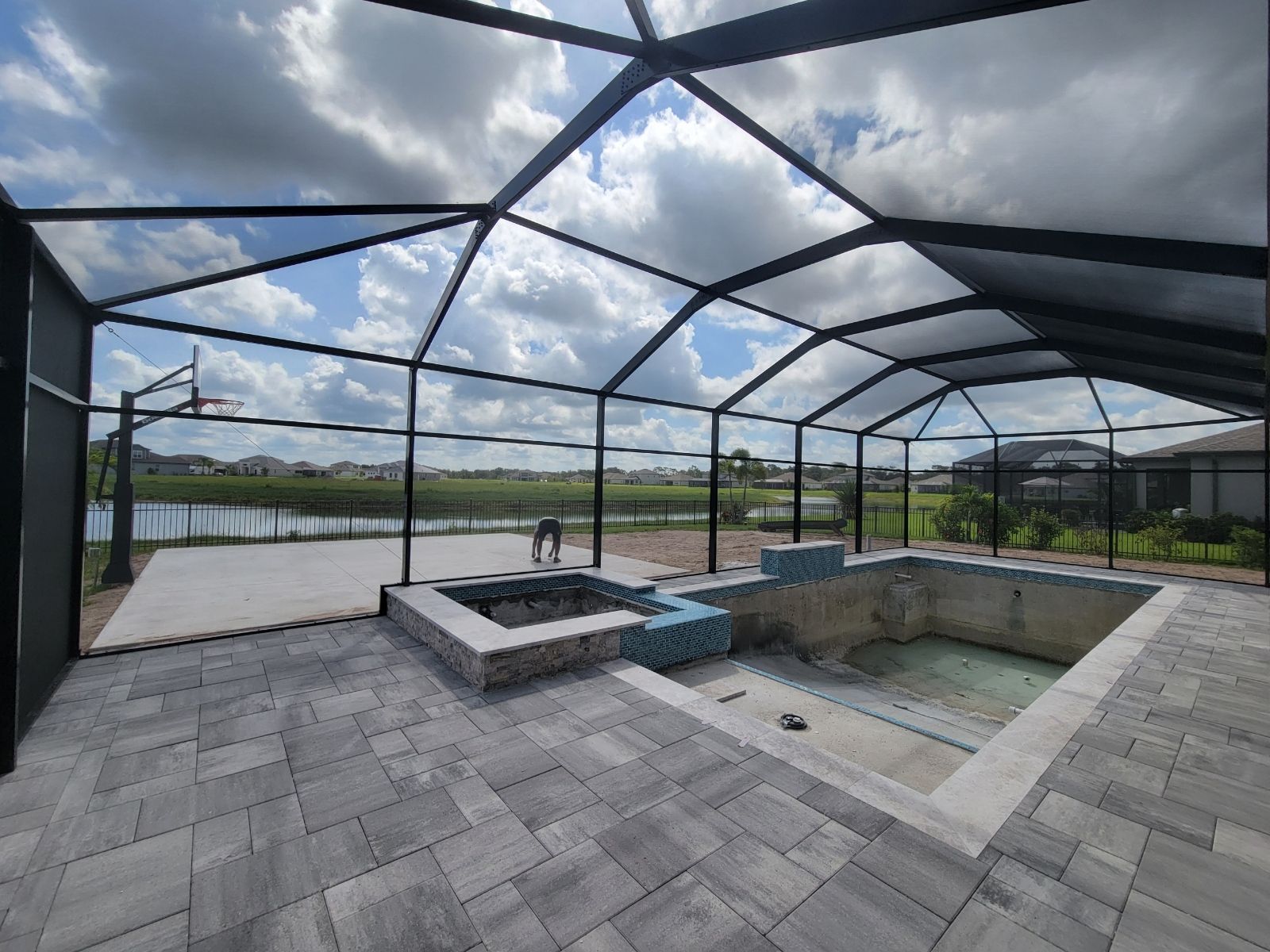 Covered patio with screened enclosure, paver floor, and empty pool and spa area under cloudy sky