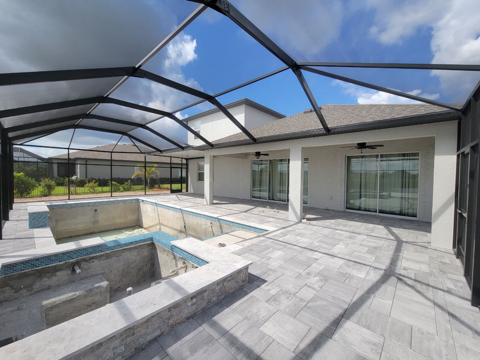 Backyard patio with screened enclosure, tiled deck, and built-in swimming pool under a partly cloudy sky