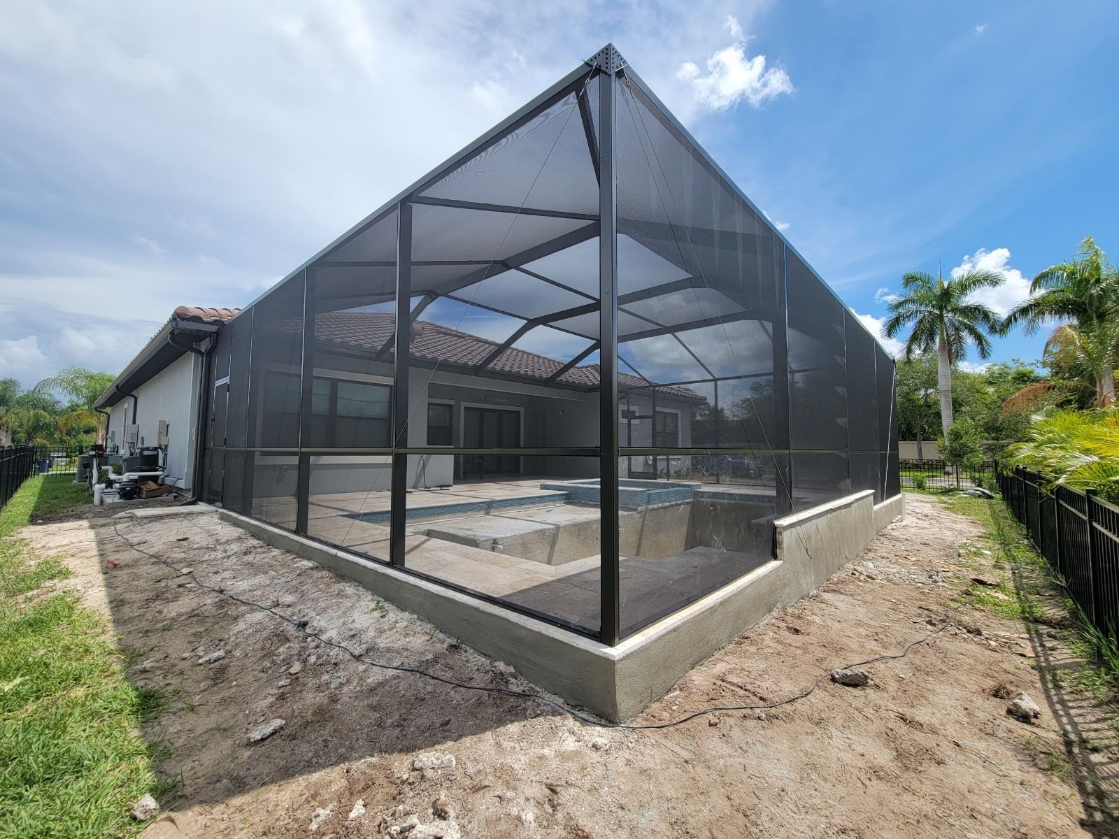 Black mesh screened enclosure around a concrete patio beside a house, under a blue sky.