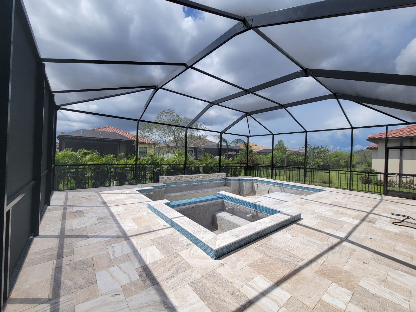 Screened patio with a small square hot tub under a cloudy sky