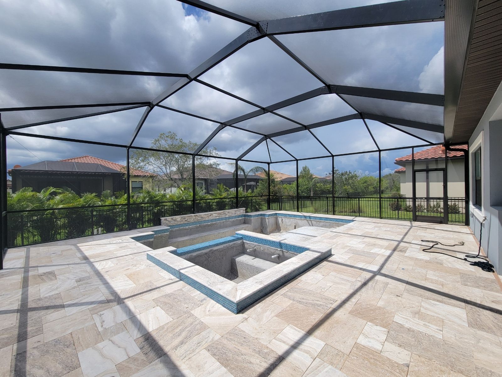 Screened-in patio with a small empty pool, stone tile floor, and cloudy sky overhead