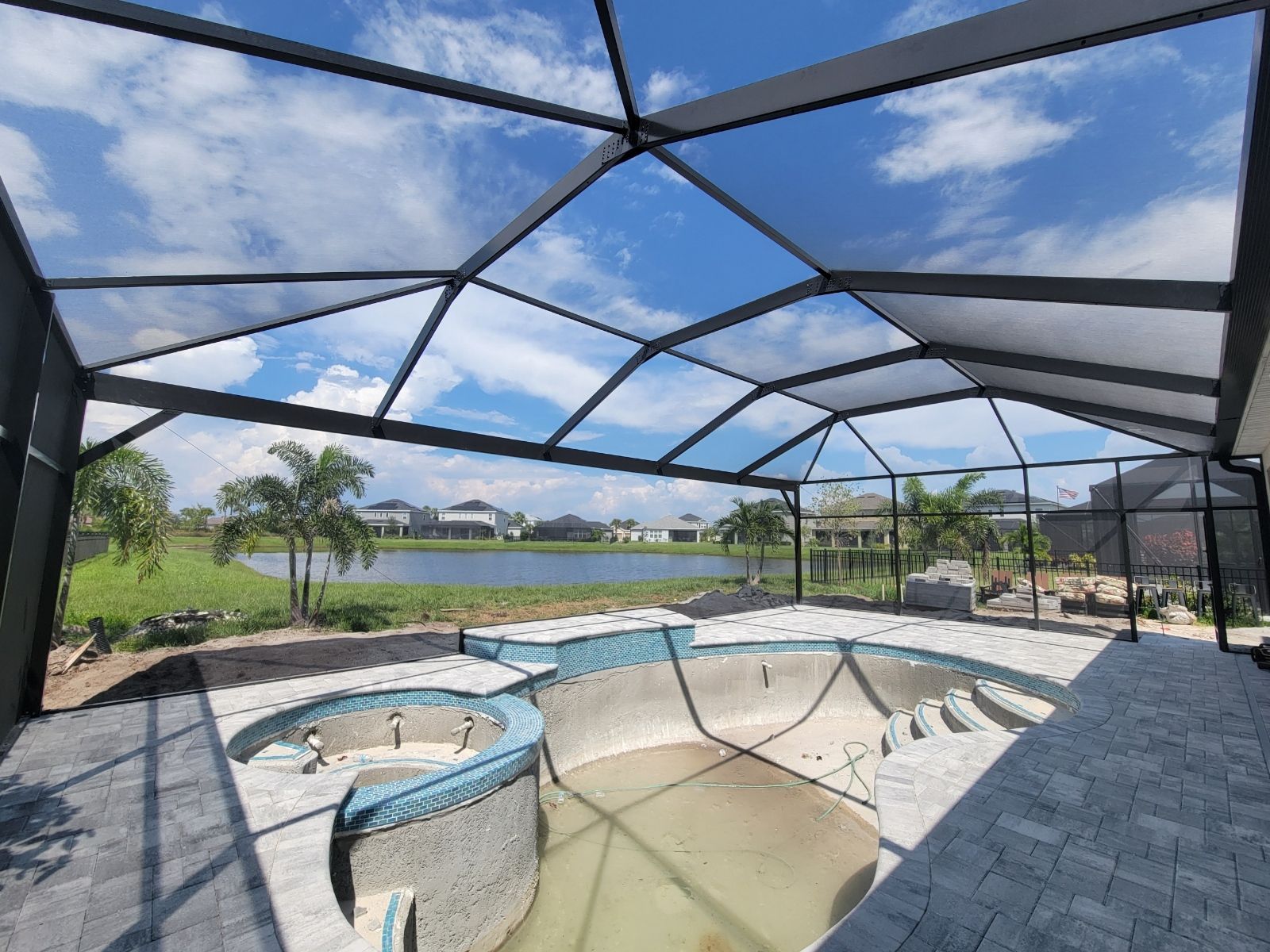 Screened-in patio with empty hot tub and pool overlooking a lake and grassy landscape
