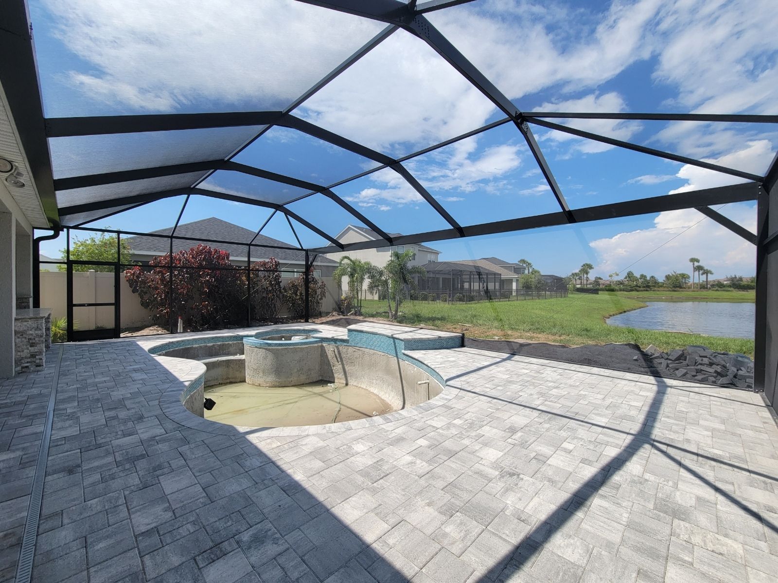 Covered patio with screened pool and spa beside a grassy backyard under a blue sky