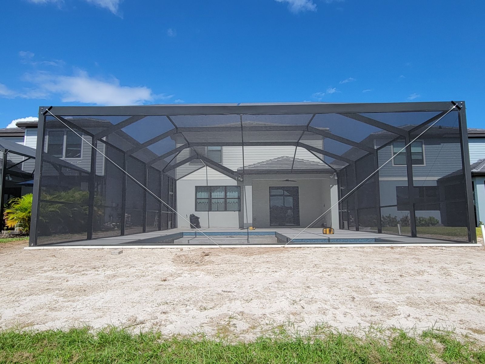 Large screened-in patio enclosure beside a house under a blue sky, on a gravel lot.