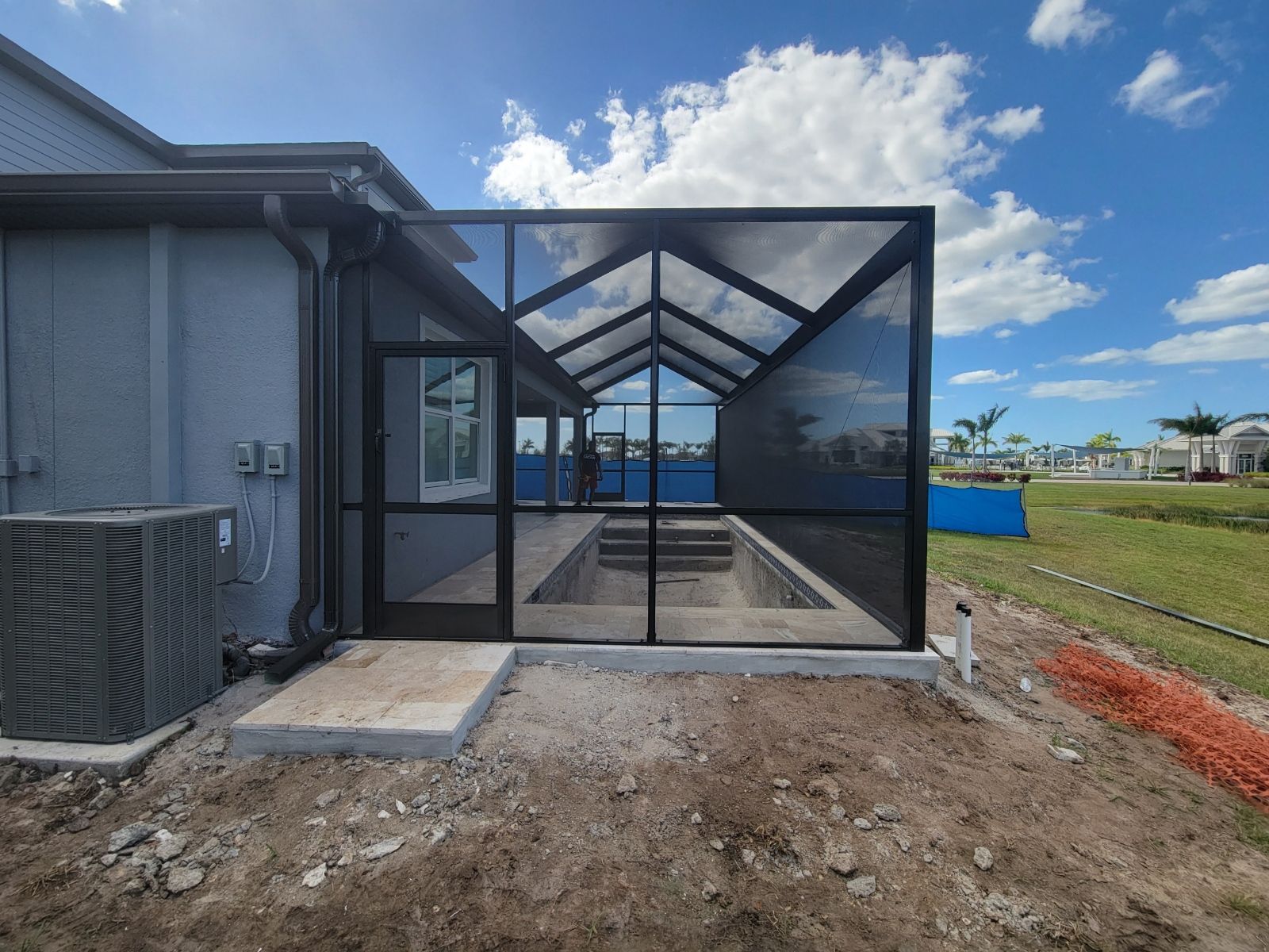 Screened back patio addition with black frame, concrete floor, and yard in front under a blue sky