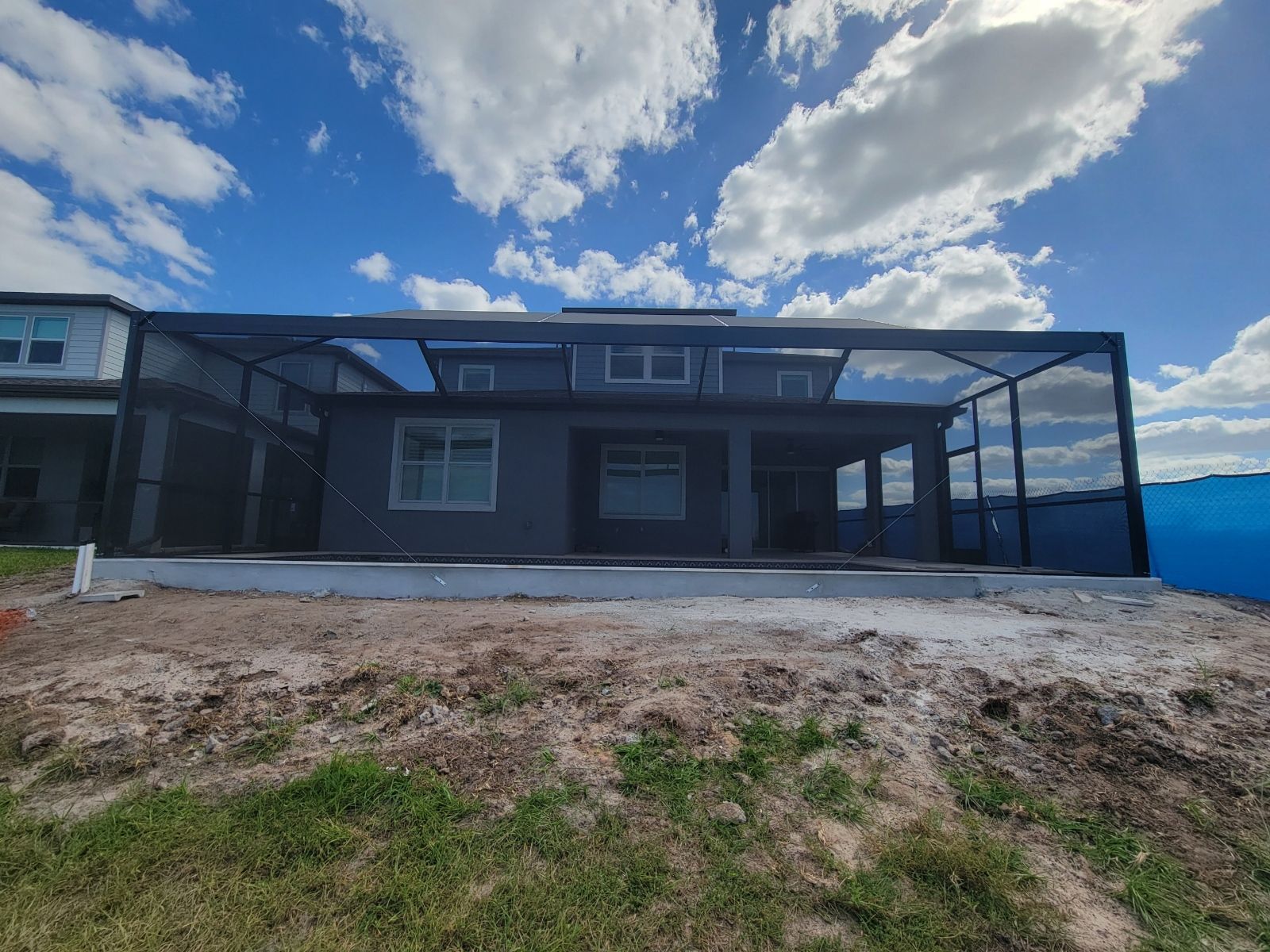 Modern single-story house exterior with a covered patio, dirt foreground, and cloudy blue sky