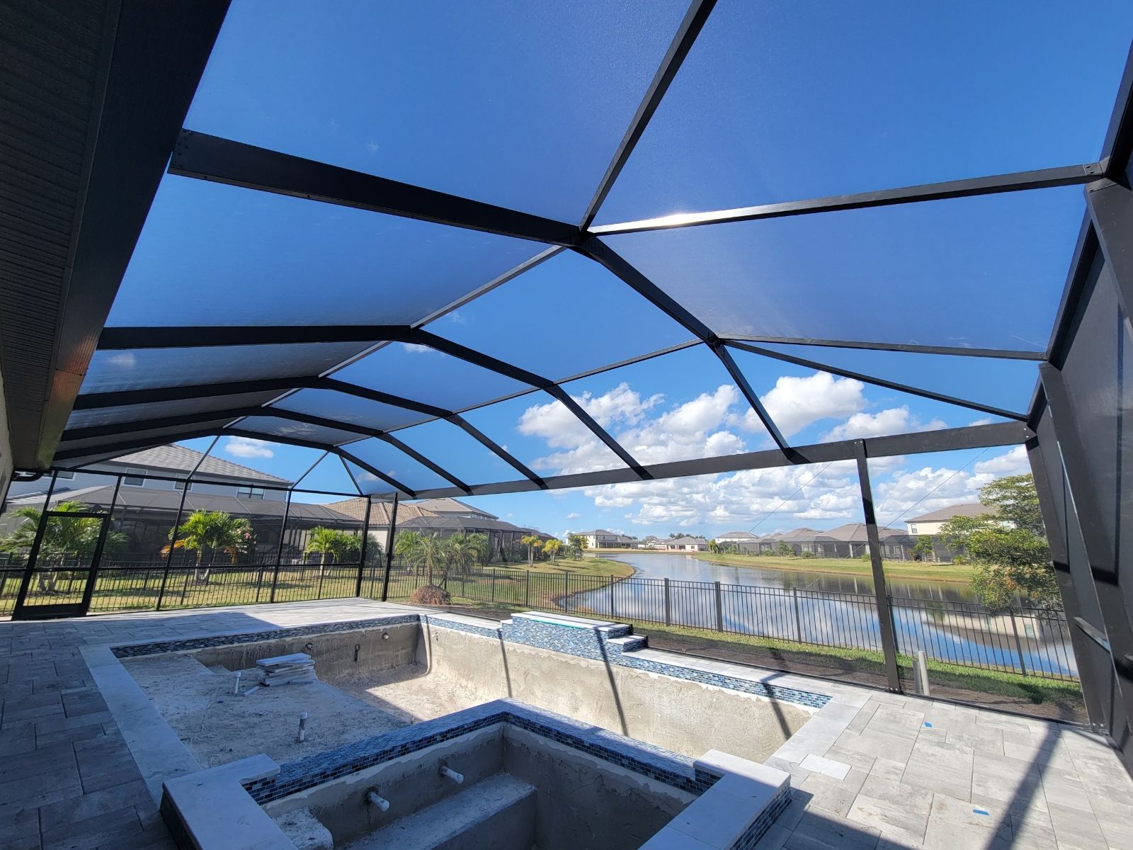 Screened backyard patio with a pool and blue sky visible through the roof panels