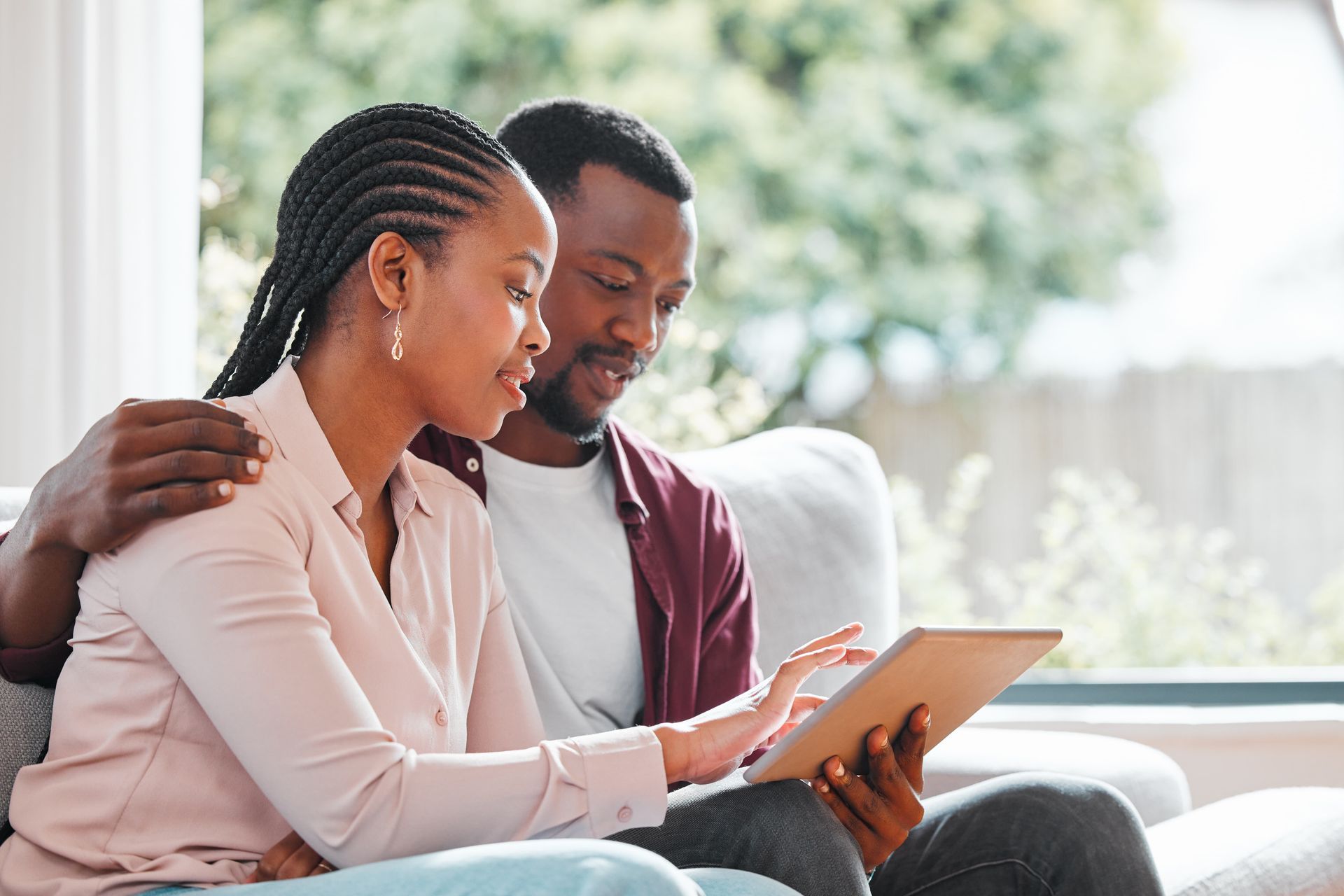 Couple sitting on a couch, smiling and looking at a tablet together in a bright living room