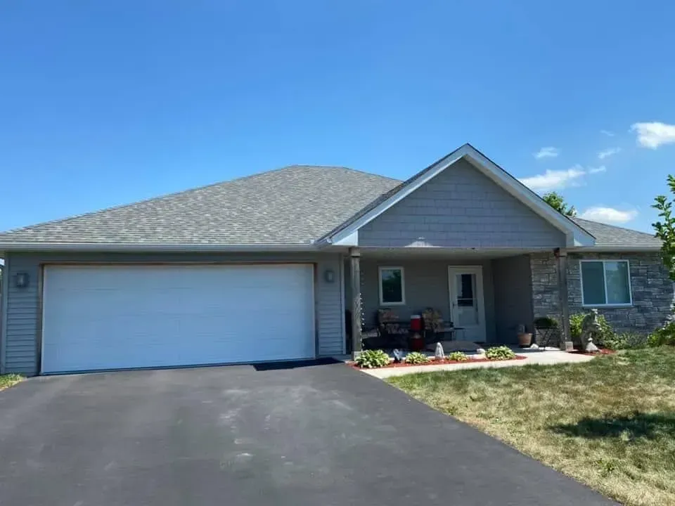 Gray ranch-style house with a two-car garage, asphalt driveway, and blue sky.
