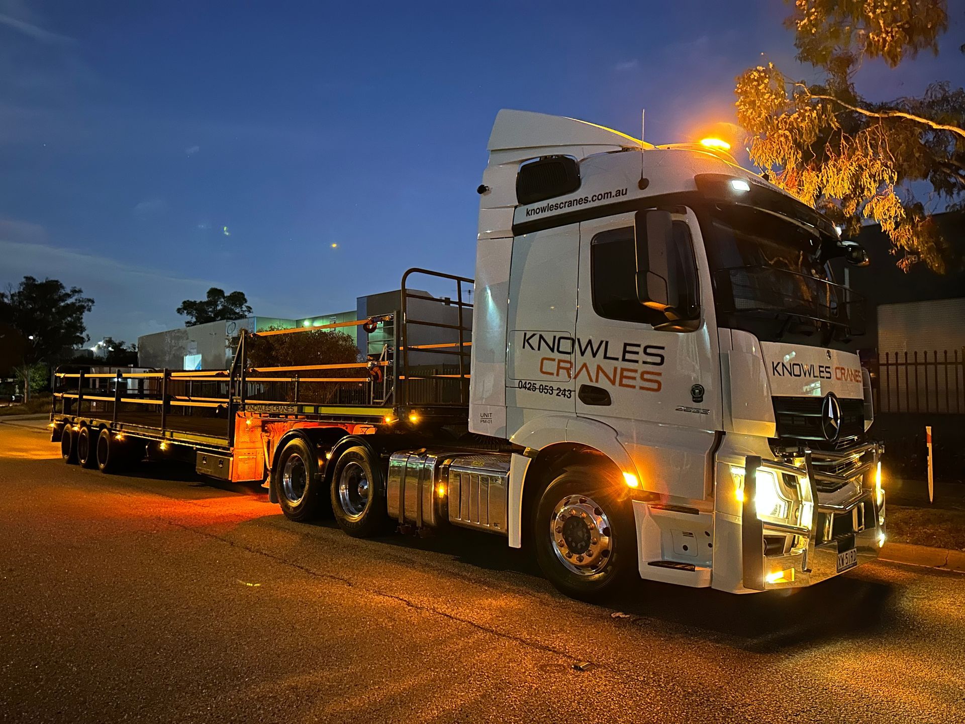 Knowles Cranes transport truck with flatbed trailer parked under evening lights.