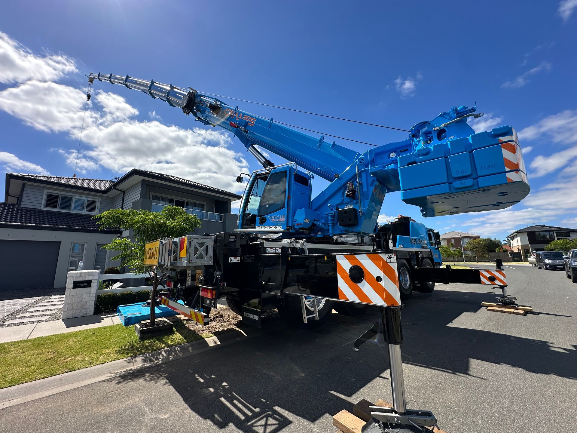 Mobile crane lifting materials at a residential site in a suburban street.