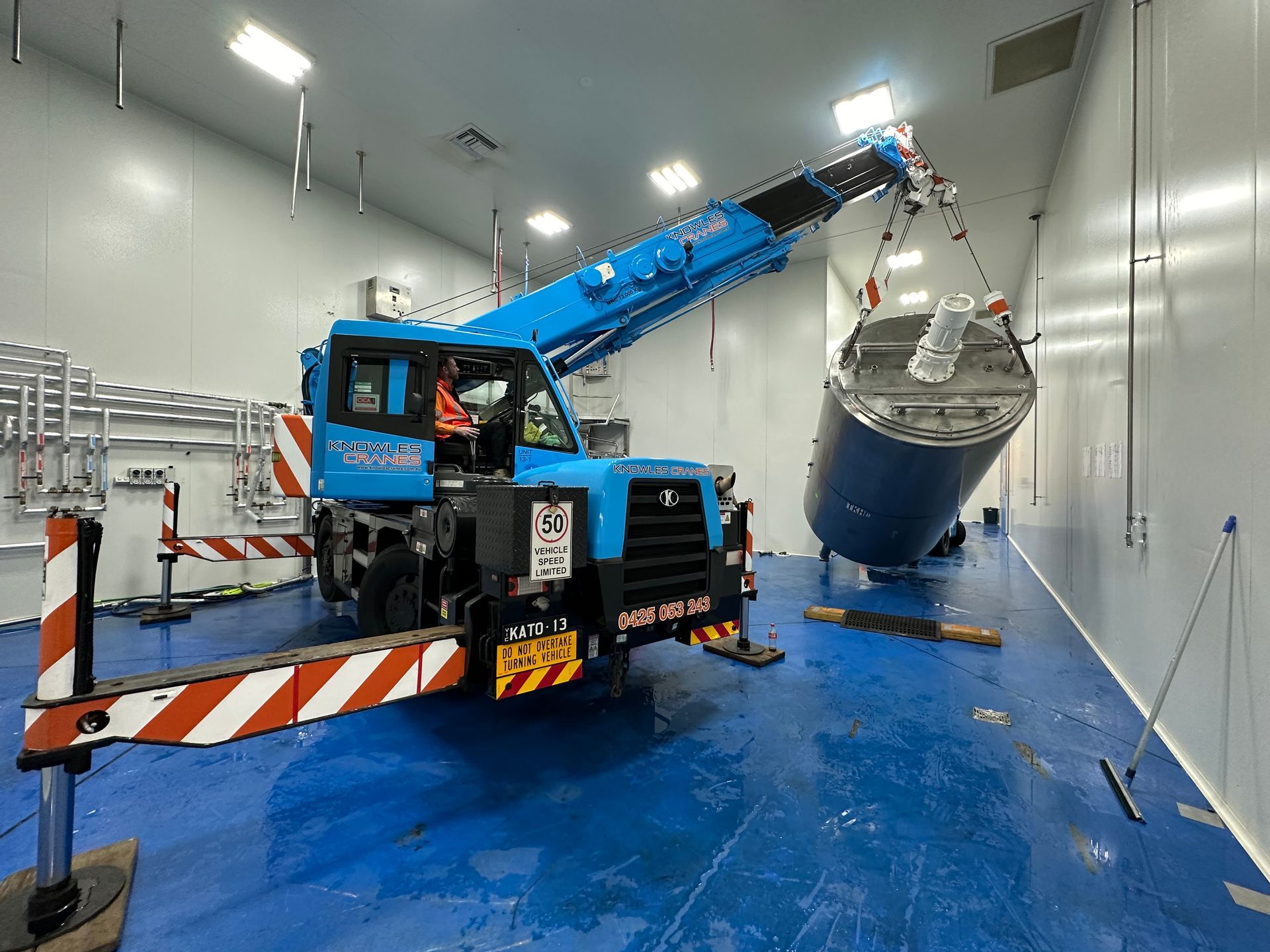 A forklift crane expertly maneuvering a heavy vessel inside a tight factory space, precision lifting in action.