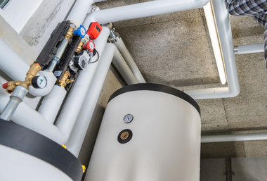 Water heater tank with pipes and gauges in a utility room.
