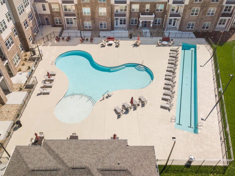 Aerial view of a complex with two pools surrounded by lounge chairs, in front of a multi-story brick building.