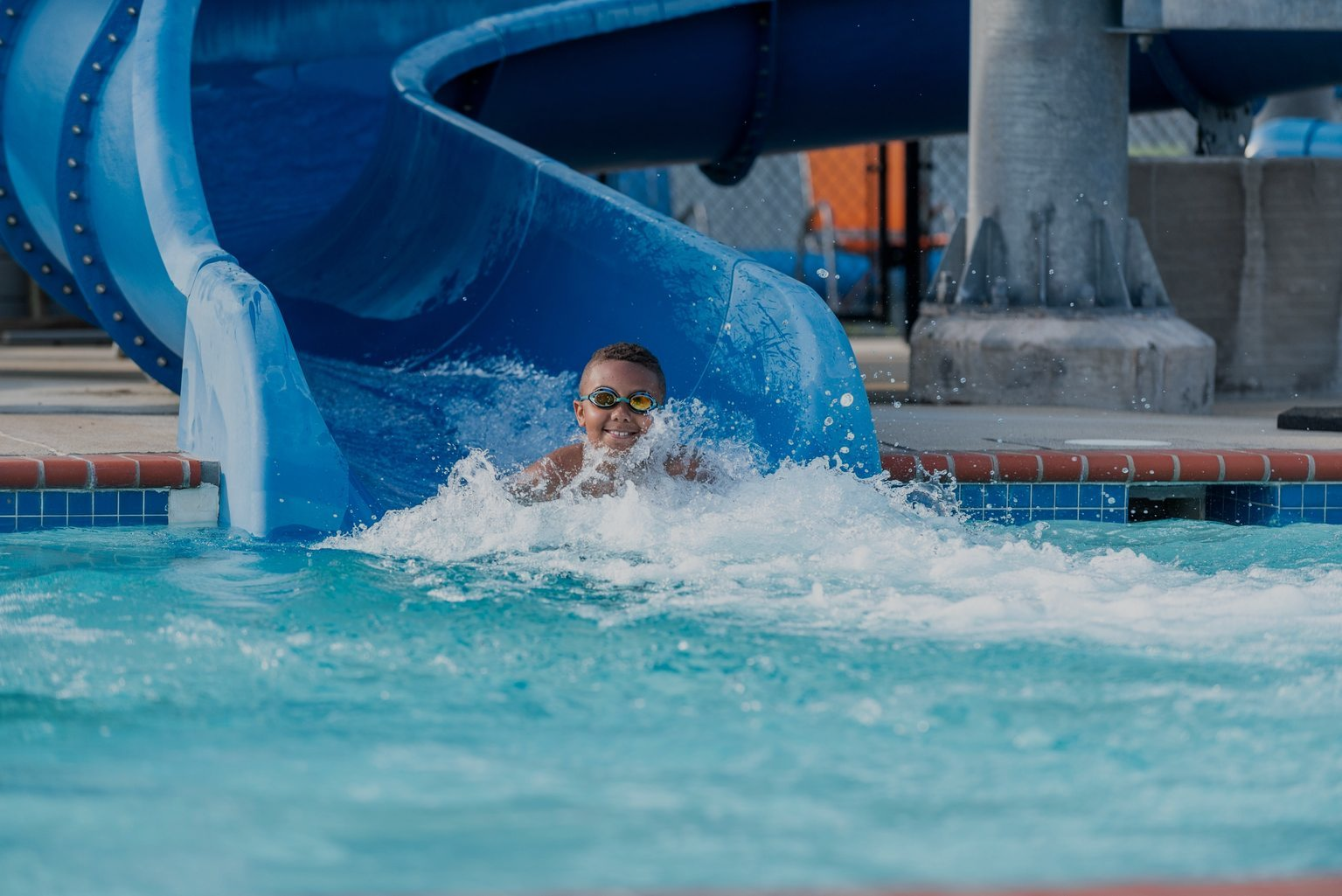 Person splashing in a pool beneath a blue waterslide